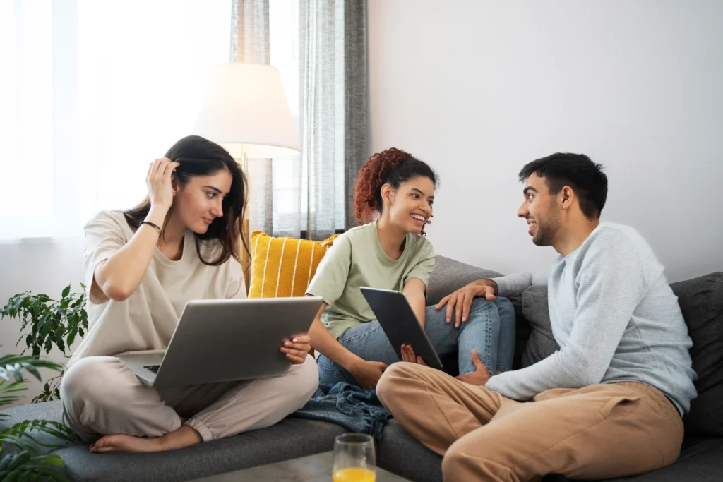 Group of young adults chatting and bonding while using digital devices at home