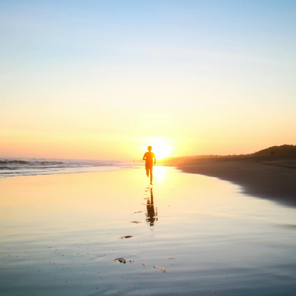 Person jogging on the beach during sunrise for a healthy lifestyle