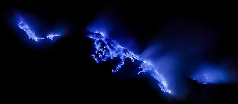Blue sulfur flames rising from Kawah Ijen volcano crater at night in Indonesia