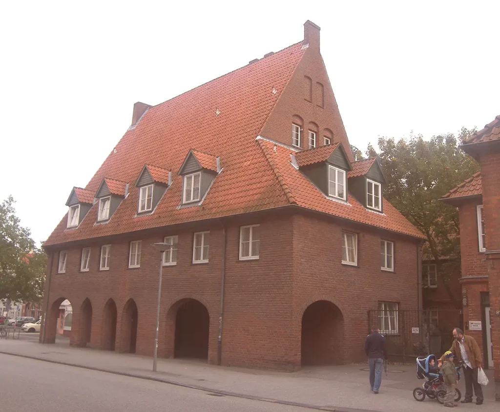 Historic brick building with a steep red roof and arched entrances, located on Wahmstrasse in Lübeck, Germany.