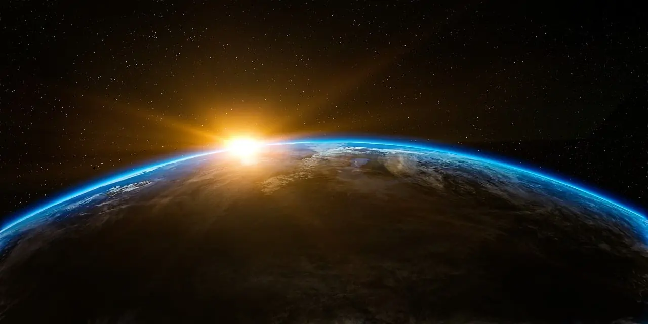 A view of a planet's curved surface with sunlight emerging over the horizon and stars in the background