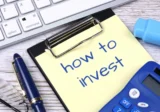 Notepad with the words “how to invest” next to a keyboard, pen, and calculator