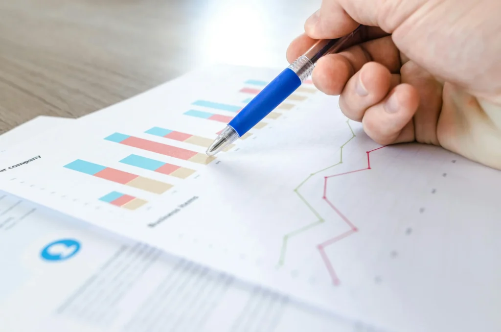 Hand holding a pen pointing at a financial chart with graphs and bar data to save money