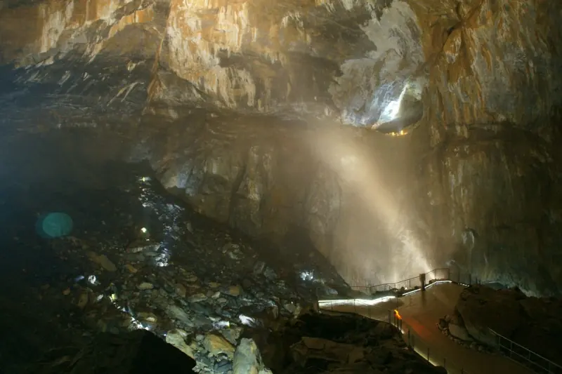 Interior view of the massive La Verna cave chamber with illuminated platform and beam of light descending from above.