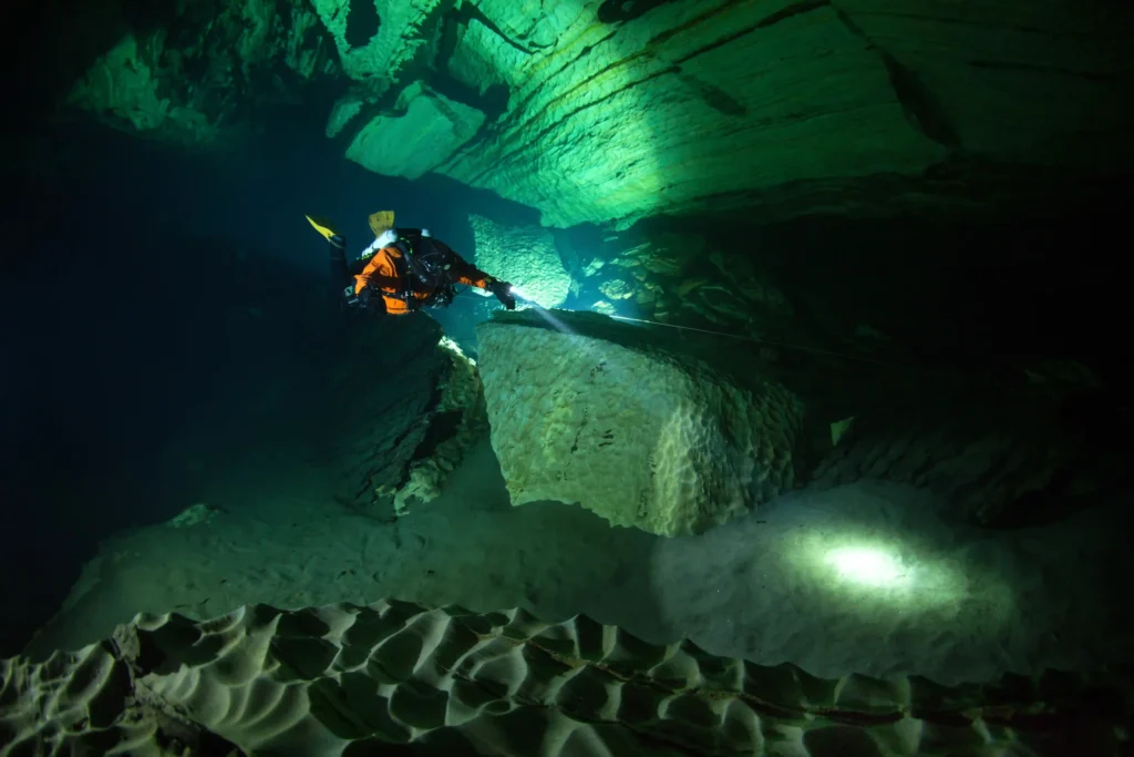 Technical cave diver with an underwater torch navigating through Pluragrotta’s marble tunnels in northern Norway.